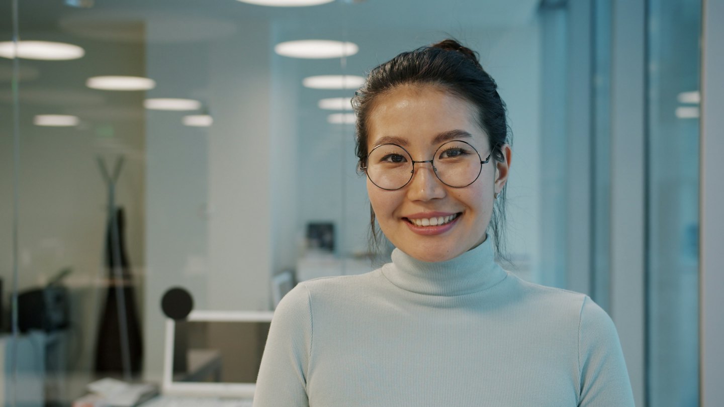 Woman wearing round glasses and a light blue turtleneck smiling.